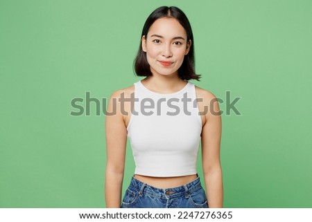 Young smiling cheerful fun happy cool beautiful woman of Asian ethnicity wears white clothes looking camera isolated on plain pastel light green background studio portrait. People lifestyle concept