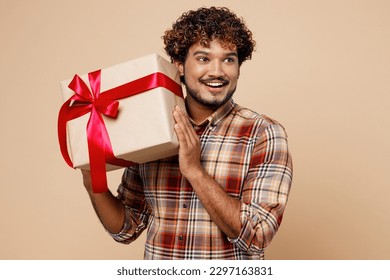 Young smiling cheerful fun Indian man wear brown shirt casual clothes hold in hand present box with gift ribbon bow look aside on area isolated on plain pastel light beige background studio portrait - Powered by Shutterstock