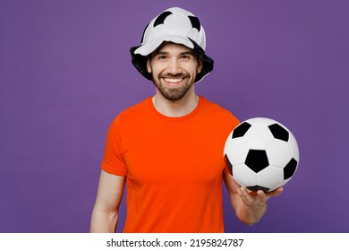 Young Smiling Cheerful Happy Cool Fun Fan Man He Wears Orange T-shirt Cheer Up Support Football Sport Team Hold In Hand Soccer Ball Panama Hat Watch Tv Live Stream Isolated On Plain Purple Background