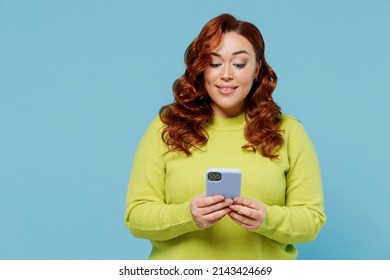 Young Smiling Cheerful Happy Fun Chubby Overweight Plus Size Big Fat Fit Woman In Green Sweater Hold Use Mobile Cell Phone Isolated On Plain Blue Background Studio Portrait. People Lifestyle Concept