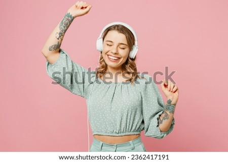 Young smiling cheerful satisfied happy woman wear casual clothes listen to music in headphones raise up hands dance isolated on plain pastel light pink background studio portrait. Lifestyle concept