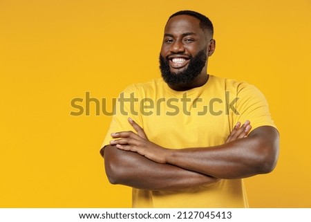 Young smiling cheerful satisfied positive happy black man 20s wear bright casual t-shirt hold hands crossed folded isolated on plain yellow color background studio portrait. People lifestyle concept