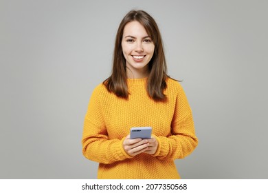 Young smiling cheerful woman 20s wearing casual knitted yellow sweater hold in hand using mobile cell phone chatting browsing typing sms messaging isolated on grey color background studio portrait - Shutterstock ID 2077350568