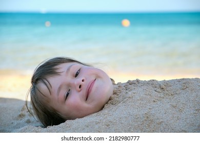 Young Smiling Child Girl Lying Down Covered With White Sand On Tropic Beach On Blue Sky And Ocean Water Background