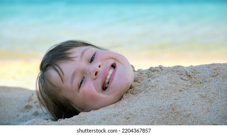 Young Smiling Child Girl Lying Down Covered With White Sand On Tropic Beach On Blue Sky And Ocean Water Background