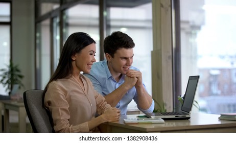 Young smiling colleagues looking laptop together sitting office table, teamwork - Shutterstock ID 1382908436