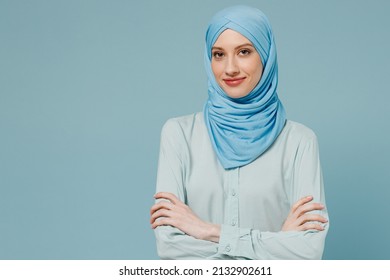Young smiling confident arabian asian muslim woman in abaya hijab hold hands crossed folded isolated on plain blue color background studio portrait. People uae middle eastern islam religious concept