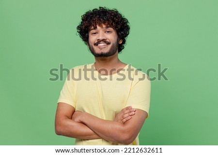 Young smiling confident happy Indian man 20s in basic yellow t-shirt hold hands crossed folded look camera isolated on plain pastel light green background studio portrait. People lifestyle concept.