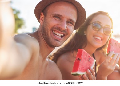 Young Smiling Couple Eating Watermelon On The Beach Having Fun, Taking Selfie, Golden Hour