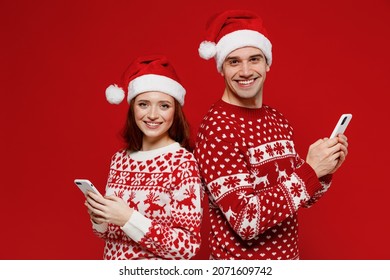 Young smiling couple friends two man woman in sweater hat hold in hand use mobile cell phone isolated on plain red background studio. Happy New Year 2022 celebration merry ho x-mas holiday concept. - Powered by Shutterstock