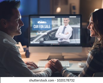 Young Smiling Couple Holding Hands And Connecting With A Computer Late At Night, They Are Buying A Car Online