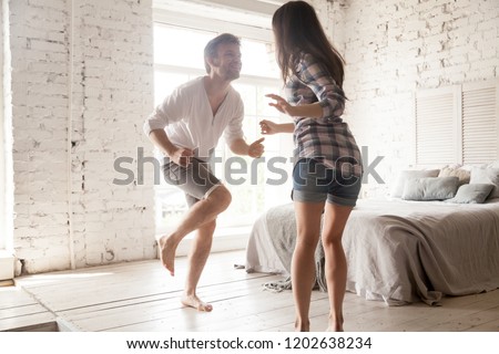 Young smiling couple in love having fun together at home in bedroom, laughing husband and attractive wife dancing on date, spending time together, enjoying, just married man and woman in new apartment