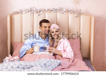 Young smiling couple in pajamas drinking coffee in the morning in the bed