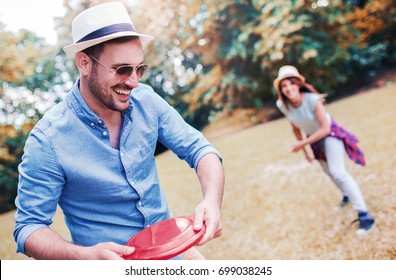 Young Smiling Couple Playing Frisbee In The Park And Enjoying In Moments Of Happiness. Sport, Recreation, Lifestyle, Love Concept