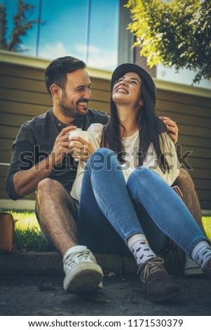 Young smiling couple sitting on sidewalk, drinking coffee. Springtime. 