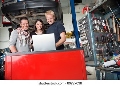 Young smiling couple standing with mechanic using laptop in auto repair shop - Powered by Shutterstock