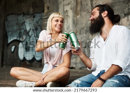 Young smiling couple toasting with beer cans in an urban environment
