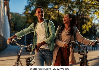 A young smiling couple is walking with their bicycles outside in the city on a sunny day. - Powered by Shutterstock