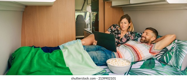 Young smiling couple watching a movie on the tablet lying on the bed of their camper van - Powered by Shutterstock