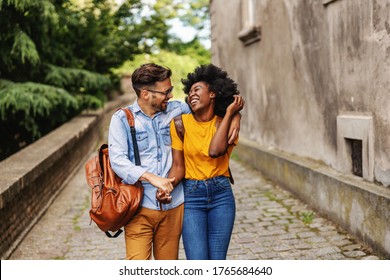 Young smiling cute multicultural hipster couple walking in an old town, hugging and flirting.