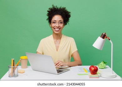 Young Smiling Employee Business Woman Of African American Ethnicity 20s Wear Yellow Shirt Sit Work At White Office Desk With Pc Laptop Isolated On Plain Green Background. Achievement Career Concept.