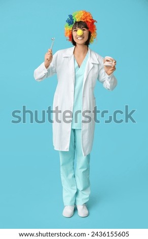Young smiling female dentist with jaw model on blue background. Fool's day