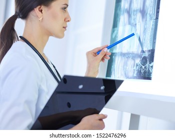 Junge lächelnde weibliche Ärztin mit Stethoskop, die in der Arztpraxis auf Röntgenstrahlen zeigt
