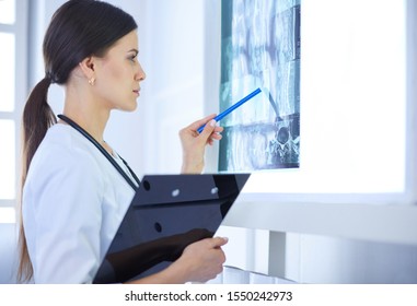 Junge lächelnde weibliche Ärztin mit Stethoskop, die in der Arztpraxis auf Röntgenstrahlen zeigt