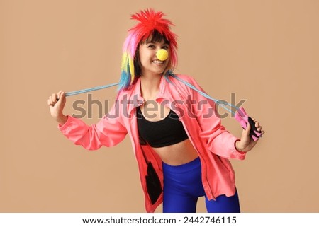 Young smiling female fitness trainer with jump rope on beige background. Fool's day