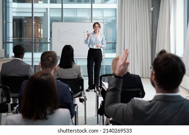 Young smiling female lecturer questioning audience after presentation of financial fluctuation graphs at seminar or conference - Shutterstock ID 2140269533