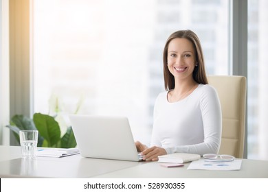 Young smiling female receptionist at the modern office desk with a laptop ready to greet clients, customers and visitors, direct them, free consultations, first impression. Looking at the camera - Powered by Shutterstock