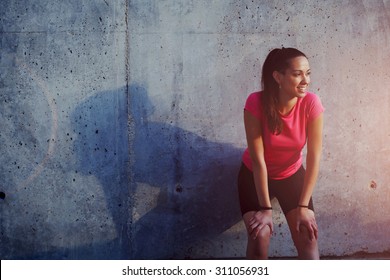 Young smiling female resting after an active fitness training while standing against gray wall with copy space area for your text message, satisfied fit woman resting after an active fitness training