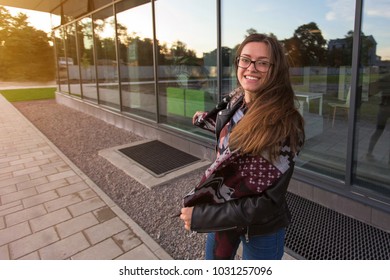 Young smiling female student near modern architecture in autumn sunset