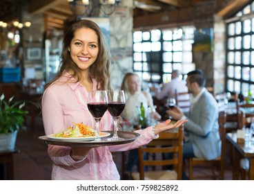 Young Smiling Female Waiter Serving Restaurant Guests
