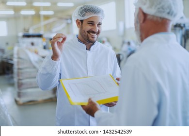 Young Smiling Food Plant Employee Talking With His Supervisor About Quality Of Food. Food Factory Interior.