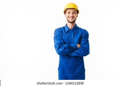 Young smiling foreman in blue uniform and yellow helmet happily looking in camera with cross hands over white background