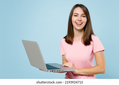 Young smiling freelancer cool happy caucasian woman 20s in pink t-shirt hold use work on laptop pc computer isolated on pastel plain light blue background studio portrait. People lifestyle concept.