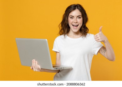 Young smiling freelancer copywriter caucasian student woman in white basic t-shirt hold laptop pc computer chat browsing show thumb up like gesure isolated on yellow orange background studio portrait