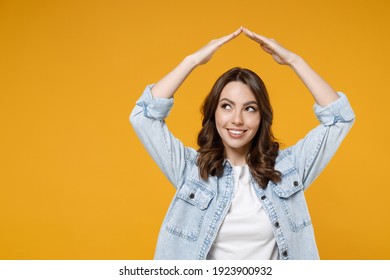 Young smiling friendly dreamful wistful fun happy woman 20s in casual denim shirt white t-shirt holding folded hands above head like house roof, stay home isolated on yellow background studio portrait