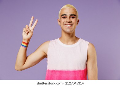 Young smiling friendly latin gay man 20s with make up wearing bright pink top showing victory sign isolated on plain pastel purple background studio portrait. People lifestyle fashion lgbtq concept