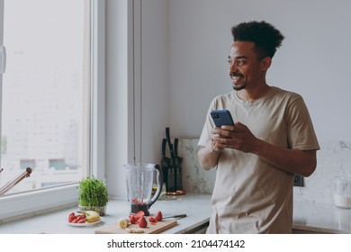 Young smiling fun african american man in casual clothes prepare fruit sweet breakfast use mobile cell phone look for recipe cook food in indoor kitchen at home alone. Healthy diet lifestyle concept. - Powered by Shutterstock