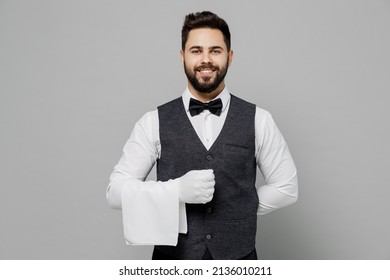 Jóvenes sonrientes y divertidos camareros hombres camareros hombres de 20 años usan chalecos blancos chalecos con elegantes guantes de uniformes en la toalla de café aislada en el retrato de estudio de fondo gris claro. Concepto de empleado de restaurante