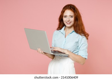 Young smiling fun consultant student businesswoman secretary redhead freelancer woman 20s in blue shirt holding laptop pc computer chat online isolated on pastel pink color background studio portrait