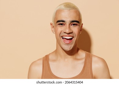 Young Smiling Fun Happy Blond Latin American Hispanic Gay Man With Make Up In Beige Tank Shirt Looking Camera Isolated On Plain Light Ocher Background Studio Portrait. People Lgbt Lifestyle Concept.