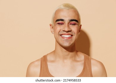 Young smiling fun happy blond latin american hispanic gay man with make up closed eyes in beige tank shirt looking camera isolated on plain light ocher background studio People lgbt lifestyle concept. - Powered by Shutterstock