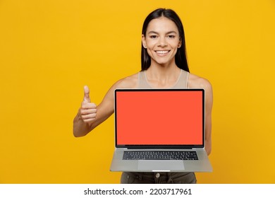 Young Smiling Fun Happy Satisfied Latin Woman 30s She Wear Basic Beige Tank Shirt Hold Use Work On Laptop Pc Computer With Blank Screen Workspace Area Show Thumb Up Isolated On Plain Yellow Backround.