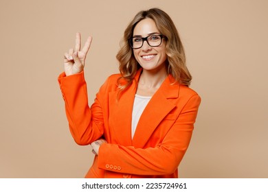 Young smiling fun happy successful employee business woman corporate lawyer 30s wear classic formal orange suit glasses work in office showing victory sign isolated on plain beige background studio