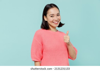 Young Smiling Fun Happy Woman Of Asian Ethnicity 20s Wearing Pink Sweater Showing Thumb Up Like Gesture Isolated On Pastel Plain Light Blue Color Background Studio Portrait. People Lifestyle Concept
