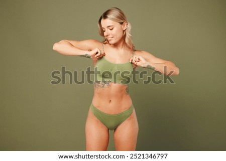 Young smiling fun satisfied nice lady woman with slim skinny body perfect skin wear top lingerie stand put hand on breast hold bra isolated on plain pastel green background. Lifestyle diet fit concept