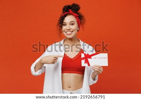 Young smiling fun surprised woman of African American ethnicity 20s wear white shirt top hold point index finger on gift certificate coupon voucher card for store isolated on plain orange background